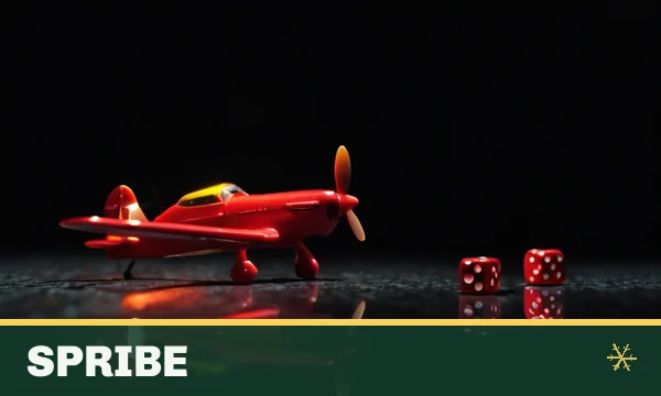 Spribe tile in the SkyFair lobby — a small red toy airplane and two dice on a dark glossy table with tiny warm lights
